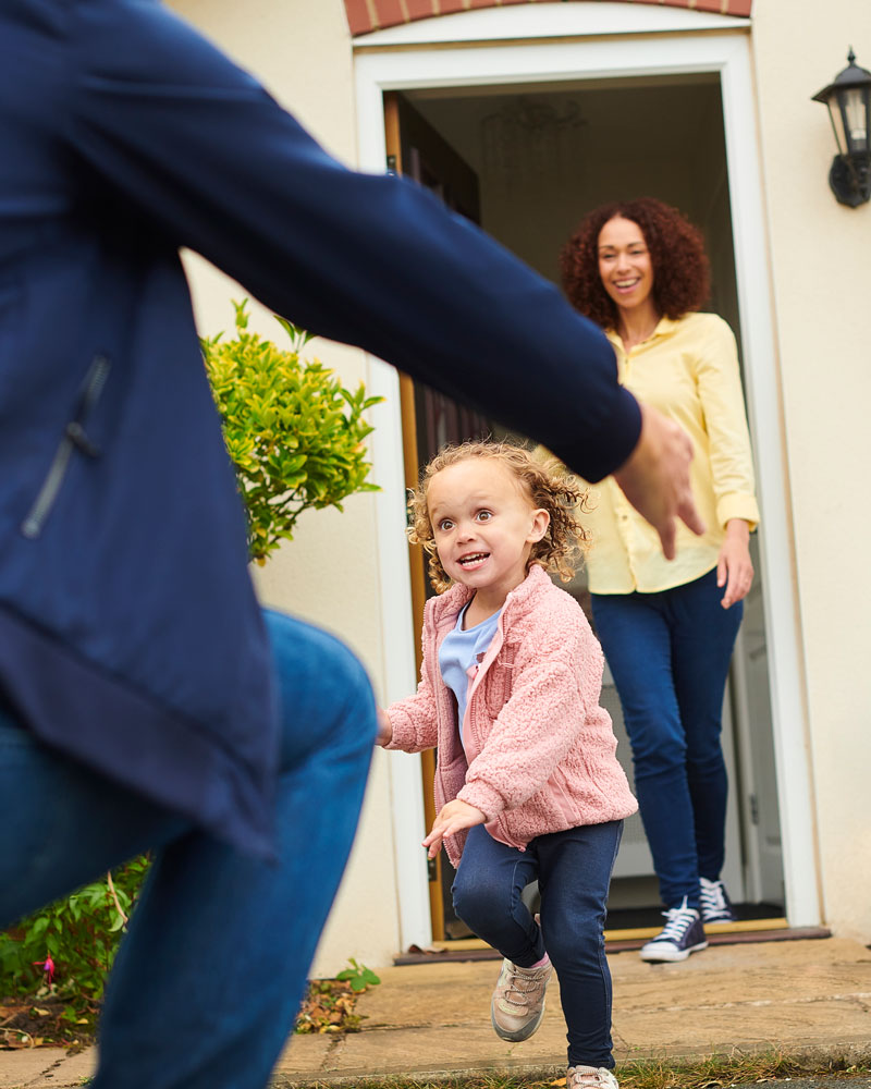 Child joyfully sprinting towards dad, with mom watching in the background, symbolizing family reunion in Los Angeles, CA