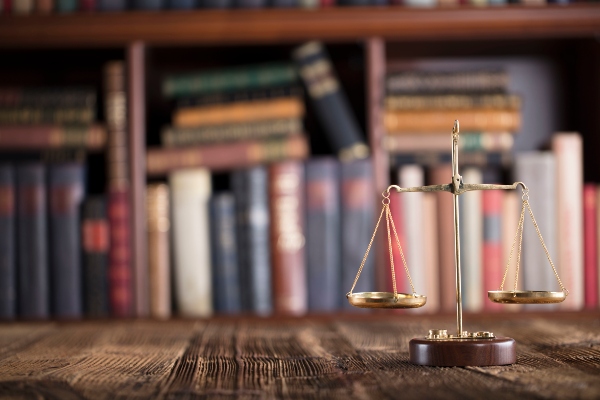 Scales of justice on a table with a bookcase full of law books behind, representing a defense lawyer's work in Ogden, UT